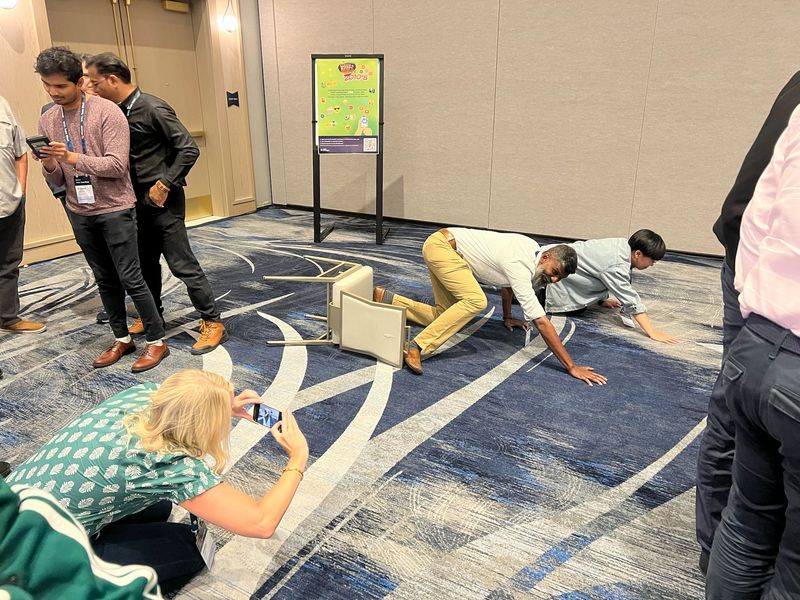 Players completing creative challenges near a Great Scott poster during an indoor event