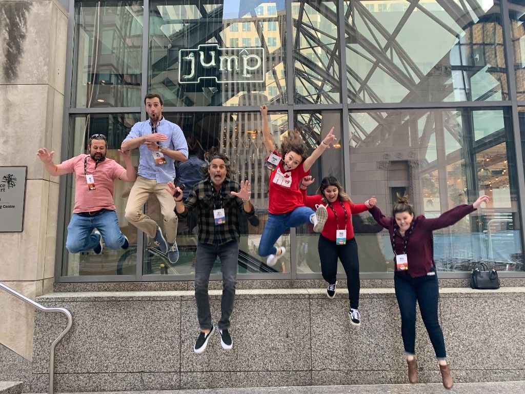 Team jumping in front of a neon jump sign